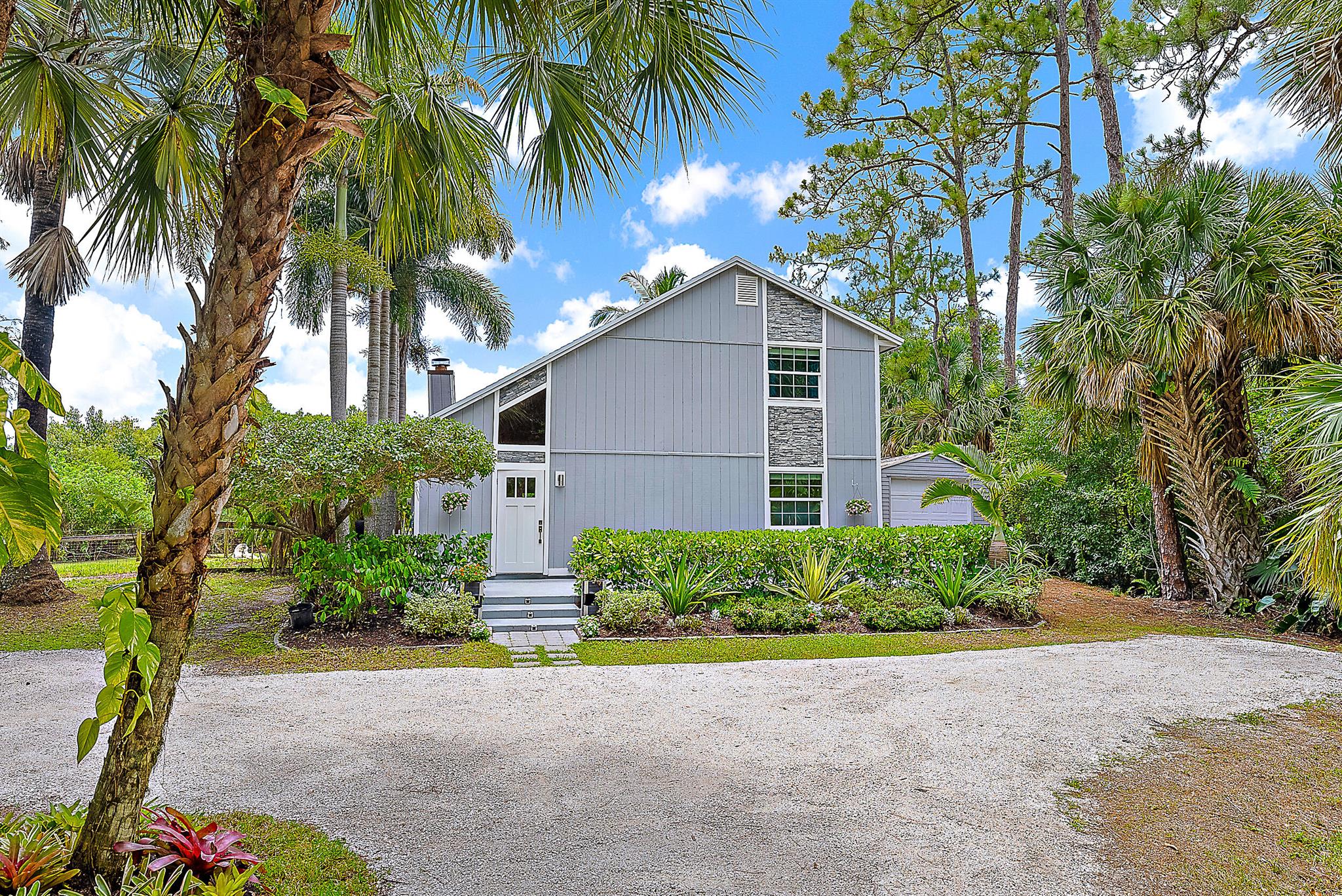Tucked away on a paved road on the desirable east side of Jupiter Farms, this property offers privacy, space, and flexibility, with a new roof completed in June 2025. The fenced backyard provides room to roam, and the pole barn can be used for animals, storage, or hobbies. A large screened-in patio overlooks the natural surroundings and offers a peaceful space to relax. There's also a detached workshop with electricity for projects or equipment.Inside, the great room is lofty and airy, anchored by a floor-to-ceiling Coquina stone fireplace. The main level includes the kitchen, dining, and living space, along with one bedroom, a full bathroom, and laundry. Upstairs are two additional bedrooms and another full bath.Zoned for top-rated schools and situated in a peaceful setting with paved road access, this Jupiter Farms location offers the best of both worlds - quiet, natural surroundings just minutes from Jupiter Farms Park, the equestrian park, miles of scenic trails, and convenient access to top parks, waterways, beautiful beaches, shopping, and dining.