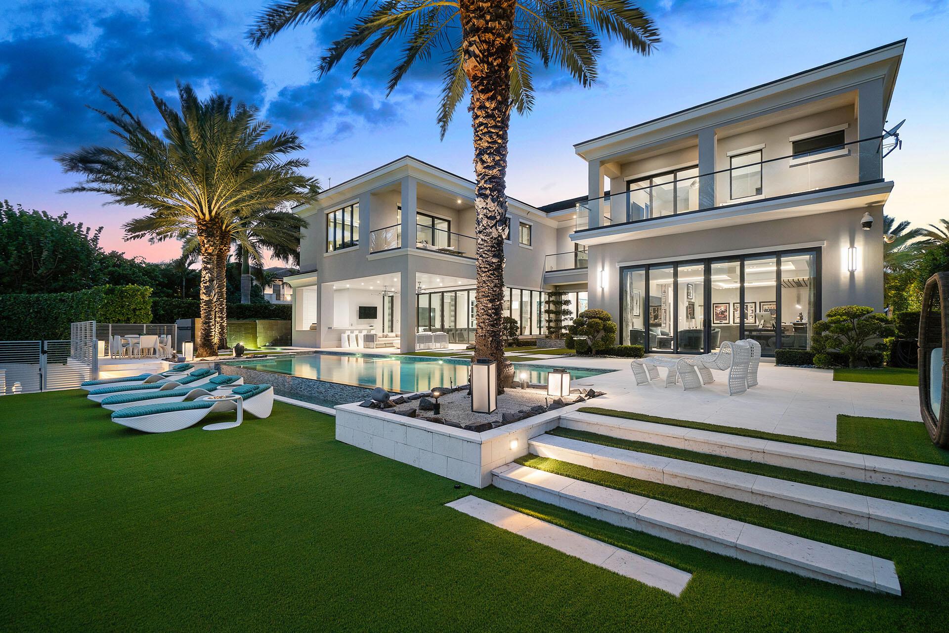 290 South Maya Palm Drive is a stunning 5-bedroom, 6.2-bathroom waterfront estate from Bloomfield Construction offering +9,000sf of modern, coastal-glam living on RPYCC's Grand Canal. The home surrounds a resort-style backyard with turf grass, infinity pool, separate spa and lanai, and all major rooms face the 110' of waterfrontage. Striking details are found throughout: a lofty 2-story gallery foyer, island with agate snack bar, floor-to-ceiling agate wall, recessed architectural lighting, floor-to-ceiling marble wall with inset gas linear fireplace, massive club room with underlit resin bar, motorized sliding glass doors leading to the covered summer kitchen, glass rail balconies with turf floors, gleaming his & her master suites with boutique closets, and 4-bay car lift capable garage.