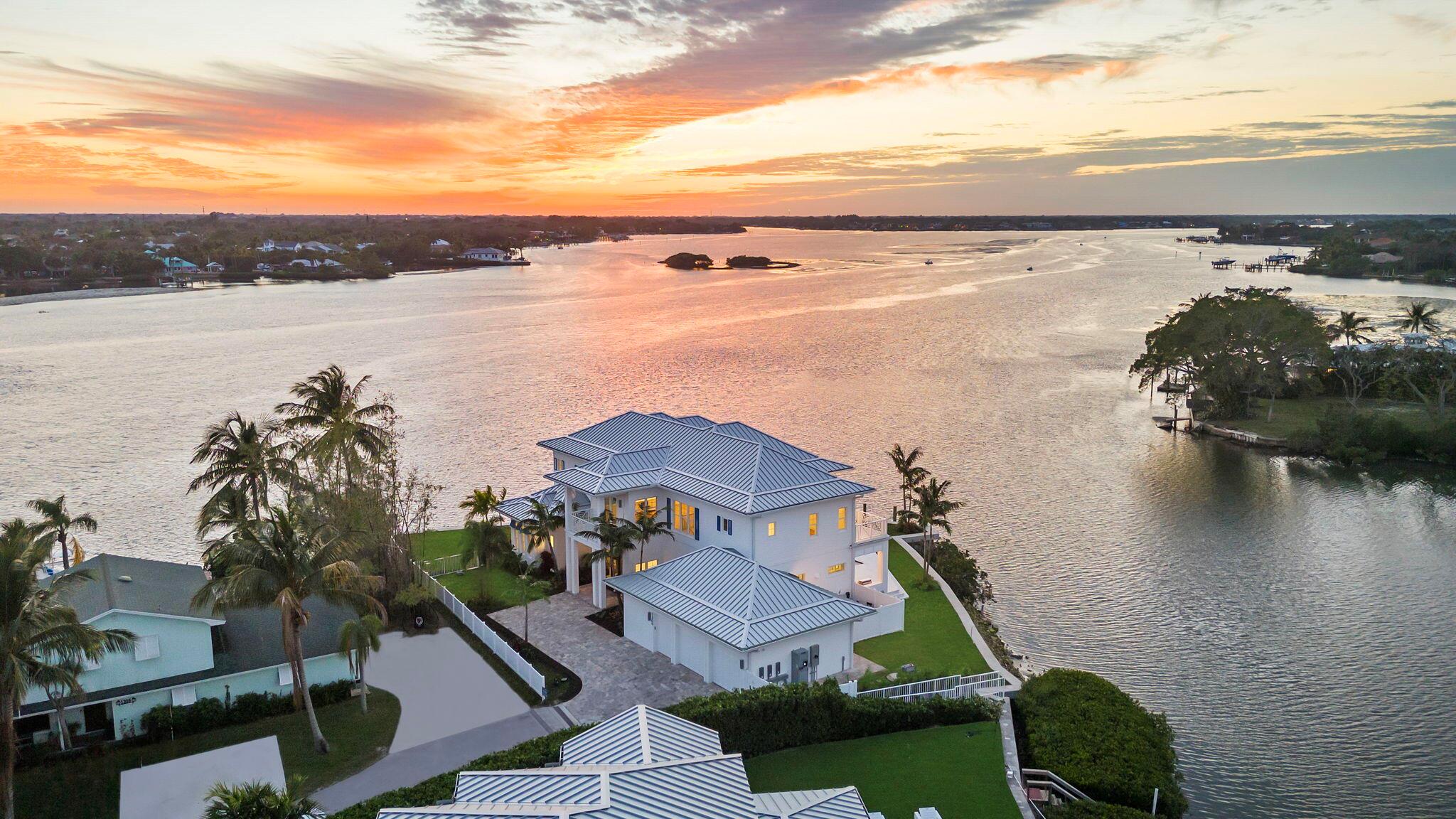 Experience the epitome of waterfront living with this dreamy sunset lover's retreat. Situated serenely along the tranquil Jupiter Inlet, this property captivates with its sprawling 265 feet of aqua-blue waterfront point lot, offering unparalleled views of the majestic Loxahatchee River. Crafted in exquisite West Indies design, this two-story new construction masterpiece showcases meticulous CBS construction from top to bottom, fortified with Icynene insulation and Acoustiblok installation. Enhanced with high-impact windows and doors, your peace of mind is assured.Within, discover the convenience of two kitchens, two living rooms, two laundry rooms and with SONO surround sound speakers. Step outside to indulge in the heated and chilled pool and spa, where every moment is framed by
