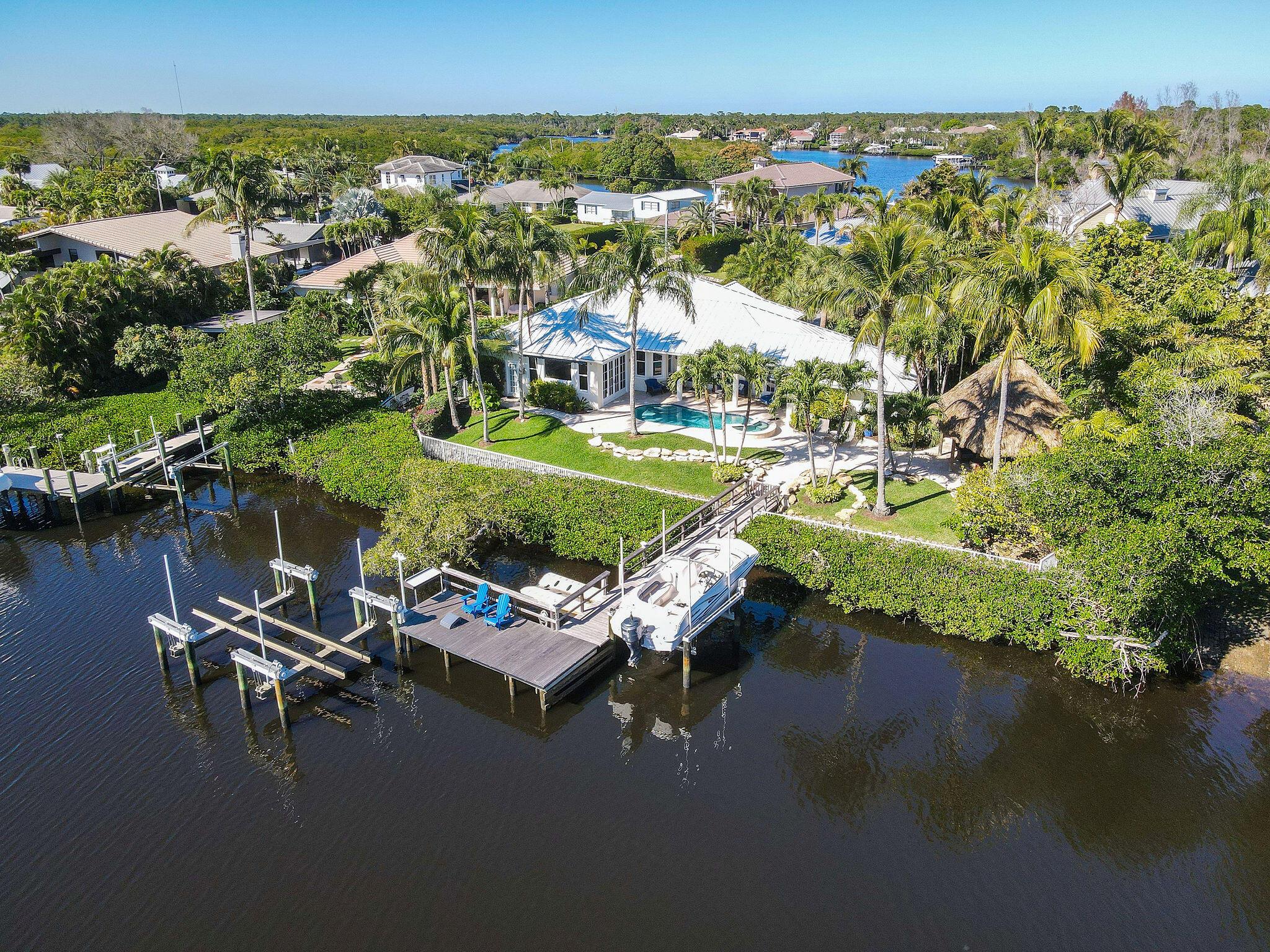 This tastefully renovated residence sits along the picturesque Loxahatchee River, offering 3 bedrooms, 3 bathrooms, 2-car garage, private pool, and spa, as well as a newer standing seam metal roof installed in 2019. The property features IPE hardwood dock complete with 9,000 lb. and 32,000 lb. lifts, along with a floating dock designed for jet skis. Outside, an expansive pool and spa area awaits, accompanied by a charming Tiki hut equipped with a large gas grill, and connections for a TV. Inside, the modern kitchen boasts top-of-the-line appliances including a Sub-Zero fridge, wine cooler, Wolff double oven and microwave, and Miele dishwasher. Impact glass windows throughout and a 32K (+/-) whole house generator ensure safety while adding convenience and peace of mind.
