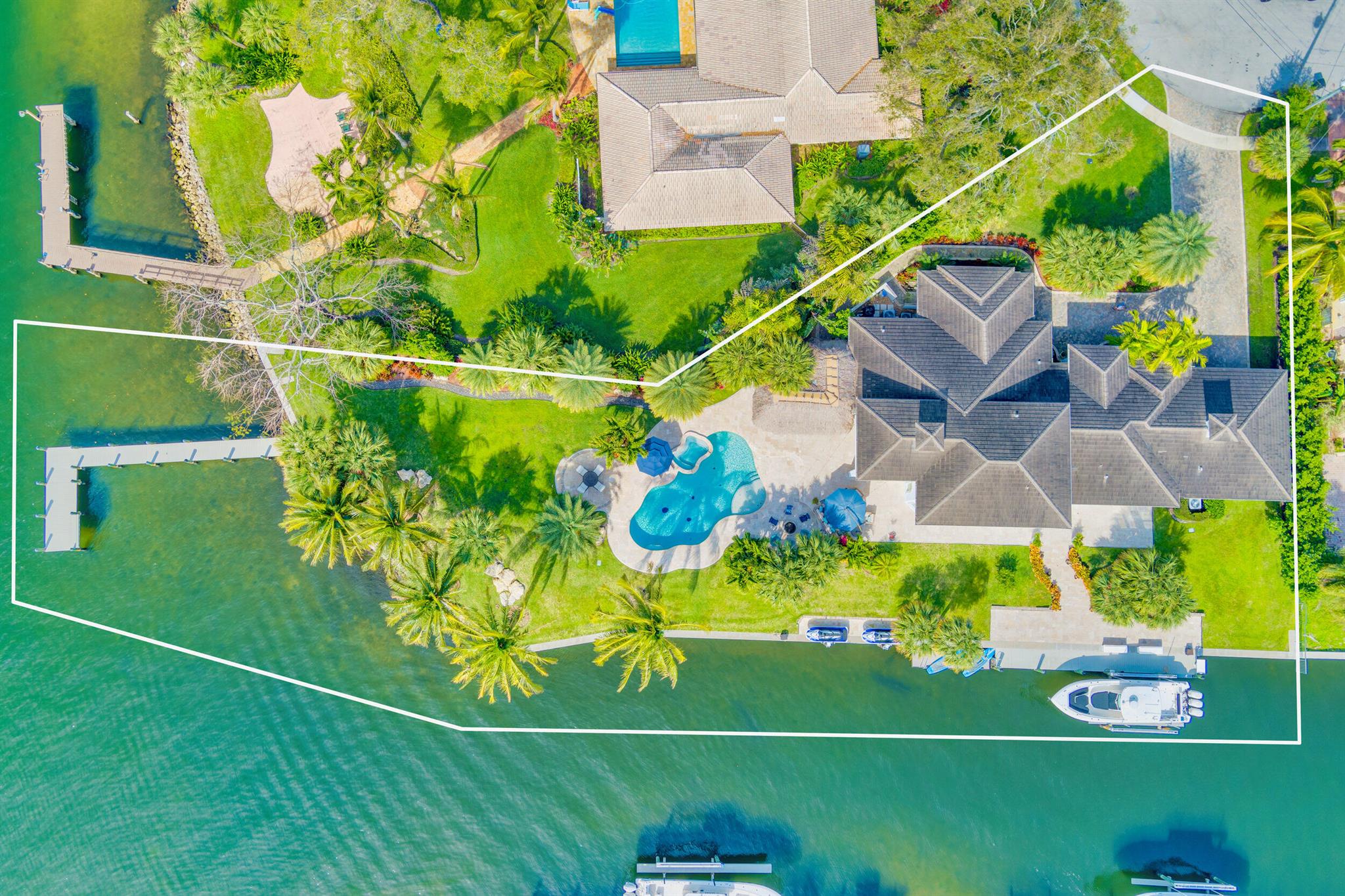 Welcome to your dream home! This rare intracoastal point property boasts unparalleled luxury and stunning waterfront views. Built in 2018, this 4-bedroom, 4-bathroom pool home offers the ultimate in waterfront living. With over 300 ft of water frontage and over 700 ft line of site across the intracoastal, this home features a deep water dock with no fixed bridges in a no wake zone, one private boat lift on a 60 ft. dock, and two jet ski lifts. Over 2,000 sq. ft of outdoor deck and walkways, you'll enjoy endless entertaining with your tiki and full outdoor kitchen. Inside, two primary bedrooms (one upstairs & one downstairs) offer privacy and comfort. The upstairs primary bedroom includes a separate living area and a big outdoor balcony where you can enjoy  spectacular sunset views. Modern finishes in the bathrooms and kitchen with high-end appliances. Porcelain tile throughout the living area with carpet in the bedrooms. Two additional bedrooms and a den/office downstairs complete this exquisite home, offering the ultimate waterfront lifestyle.