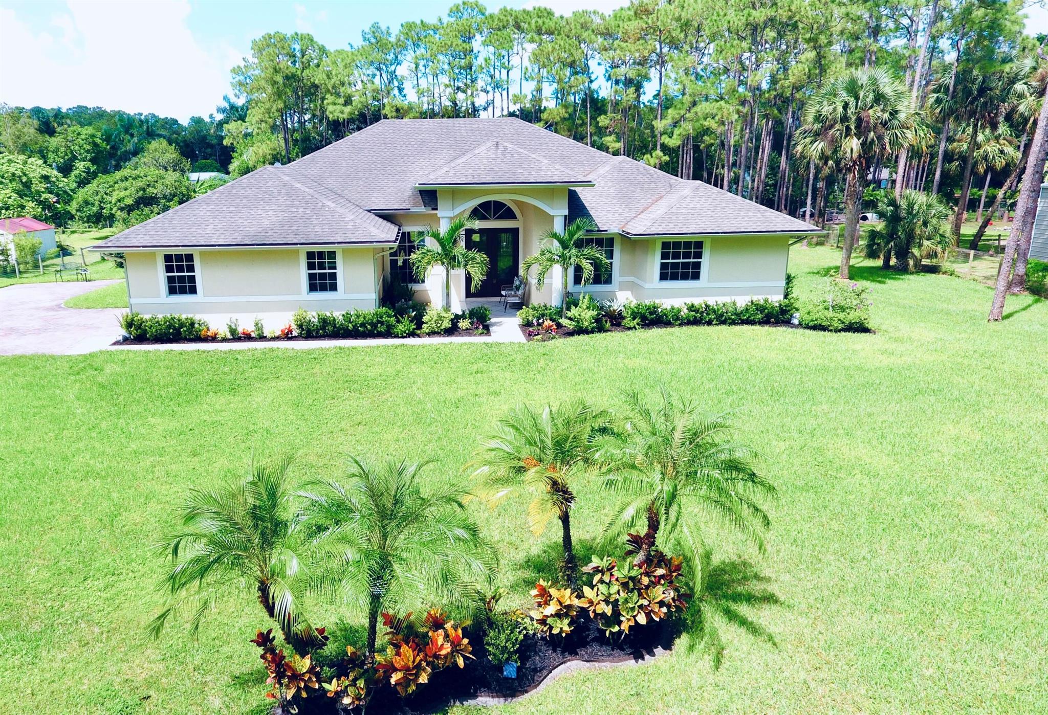 This exquisite Jupiter Farms residence, constructed in 2015, presents an impressive combination of modern luxury and timeless elegance. Set on a sprawling 1.25-acre lot, this home features 5 bedrooms, 3 bathrooms, and a 2-car garage, offering ample space and privacy. The property's gated entrance and pavered driveway set the stage for a warm and welcoming arrival experience. As you approach the covered front patio and step inside, you'll immediately notice the open floor plan, designed to maximize both space and natural light. The home features soaring 11-foot ceilings, intricate crown molding, and elegant 8-foot doors throughout, creating an airy and sophisticated ambiance. The formal living and dining rooms offer beautiful views of the outdoor living area, enhancing the home's connection to its natural surroundings. The kitchen is a true highlight, designed to be both functional and stylish. It boasts custom cherry cabinets, stainless steel appliances, and luxurious granite countertops. A spacious pantry and a generously sized island with a snack bar provide ample storage and preparation space. Adjacent to the kitchen, the breakfast nook is perfect for casual meals, while the adjoining family room is designed for relaxation and socializing. Sliding glass doors seamlessly connect the indoor space with the covered lanai, making it ideal for entertaining or enjoying a quiet moment outdoors. The master suite is a serene retreat, thoughtfully designed to offer comfort and privacy. It features French doors that open directly onto the lanai, providing lovely views of the expansive backyard. The en-suite bathroom is equipped with dual vanities, a separate tub and shower, and his-and-her closets, all contributing to a spa-like atmosphere. In addition to the master suite, the home includes four additional bedrooms. Two of these bedrooms share two well-appointed bathrooms, while the fifth bedroom, which includes a closet, can easily be used as an office or den, offering flexible living options to suit your needs. This residence is also equipped with several high-quality features designed for both convenience and safety. Hurricane impact doors and windows provide peace of mind, while the indoor laundry room adds to the home's practicality. The side-load 2-car garage is located on a paved street, enhancing both functionality and aesthetic appeal. Additional features include a Walter filtration system, a security system, and a sprinkler system, all contributing to the property's overall quality and convenience. The home's exterior spaces are just as thoughtfully designed as the interior. The covered lanai provides a comfortable space for outdoor relaxation and entertainment, seamlessly blending with the indoor living areas. Beyond the lanai, the vast backyard awaits your creative vision. This expansive outdoor space is a blank canvas, offering endless possibilities for you to design your ideal retreat. Whether you envision a tranquil garden, a sparkling pool area, or an extensive entertainment zone, this property provides the perfect foundation to bring your outdoor dreams to life. In summary, this Jupiter Farms home combines modern amenities with elegant design, set in a peaceful and private location. Its spacious interior, luxurious master suite, and versatile additional bedrooms provide a comfortable and functional living environment. The well-appointed kitchen and open floor plan are ideal for both everyday living and entertaining, while the expansive backyard offers endless opportunities for customization. With its impressive features and serene setting, this residence is not just a house, but a true home ready to offer its new owners both comfort and joy.