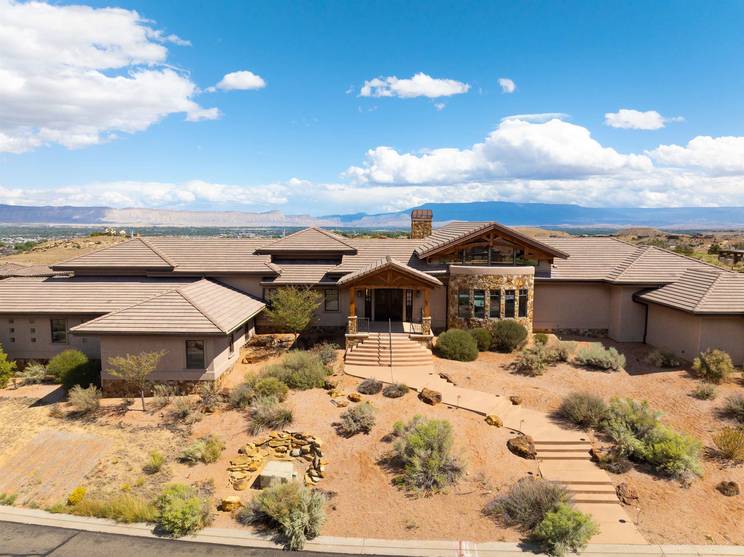 Sprawling luxury estate with majestic views at the award-winning Redlands Mesa Golf Course!  Situated on 2 combined lots, this iconic craftsman stone and wood home with over 6,100sf, was constructed with views of the Grand Valley and Colorado National Monument in mind.  Splendid grandeur exudes as you enter the large foyer that leads you to the heart of the home.  The gourmet kitchen with built-in breakfast nook, walk-in pantry, 2 islands, 2 sinks and desk area opens up to a 2 story great room with a full height stone fireplace, stately timber trusses, cathedral ceilings and a wall of windows. The designer renovated primary suite is a one-of-a kind sanctuary with three separate yet adjoining areas including 3 fireplaces, double closets, laundry area, modern kitchenette and a luxurious spa-like bathroom. Four bedrooms with adjoining bathrooms, oversized mudroom, office and dining area are just some of the many features throughout the sizeable home. The walk out basement includes a full kitchen, bathroom and laundry area that opens up to the in-ground pool, several tiered patios and fireplace with stunning views.