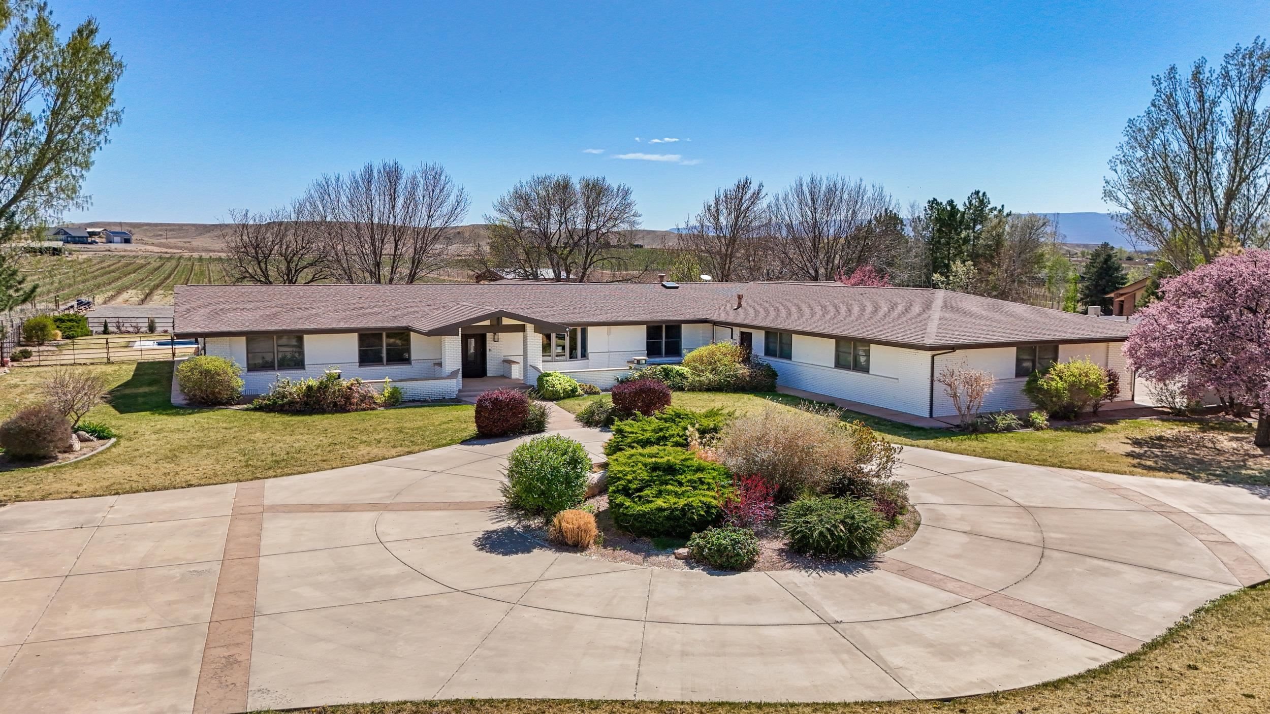 Welcome to your dream retreat on East Orchard Mesa—where luxury meets lifestyle on 7 irrigated acres surrounded by orchards and vineyards. This custom brick ranch offers privacy, panoramic views of Mt. Garfield and the Grand Mesa, and a rare in-ground pool! A grand circular driveway welcomes you to the beautifully landscaped grounds. Step inside to discover a stunning and expansive open-concept layout featuring vaulted ceilings, a custom stone fireplace, and a chef’s kitchen equipped with quartz countertops, Thermador stainless steel appliances, and a spacious butler’s pantry. The kitchen flows seamlessly into the formal dining area and great room, ideal for entertaining. The main level includes three generously sized bedrooms, each with its own ensuite bath. One suite offers private exterior access and can be locked off from the rest of the home—an ideal setup for a guest suite, or multigenerational living. Downstairs, the fully finished basement includes a large rec room and two additional bedrooms (one non-conforming). Step outside to your expansive patio with a custom pergola, overlooking a beautiful lawn, sparkling in-ground pool, and sweeping views of your 7-acre estate. Approximately 4 acres are newly planted with 3rd-leaf sweet cherries and wine grapes—an ideal setup for anyone dreaming of a boutique orchard or vineyard operation. The property also includes a well-equipped horse barn with electric service and an evaporative cooler, along with a separate metal pole barn and tack room—offering versatility for future agricultural use, hobby farming, or storage. With senior water rights for all 7 acres and 400 amps of power already in place near the pole barn, the property is perfectly positioned for everything from modern agricultural ventures to high-end recreational amenities or guest accommodations. Additional features include an oversized heated 4-car garage, solid core doors throughout, prep sink in kitchen and pantry, and a hobby vineyard planted with table grapes. This exceptional property is being offered on its own or in combination with the adjacent 11.8-acre parcel to the south, which is planted in 3rd-leaf Palisade peaches—providing a rare opportunity to expand your footprint in Colorado’s most sought-after agricultural region. Whether you're looking for a turnkey orchard operation, a luxury farmstead, or an investment in fruit and wine country, this is a legacy property with limitless potential.