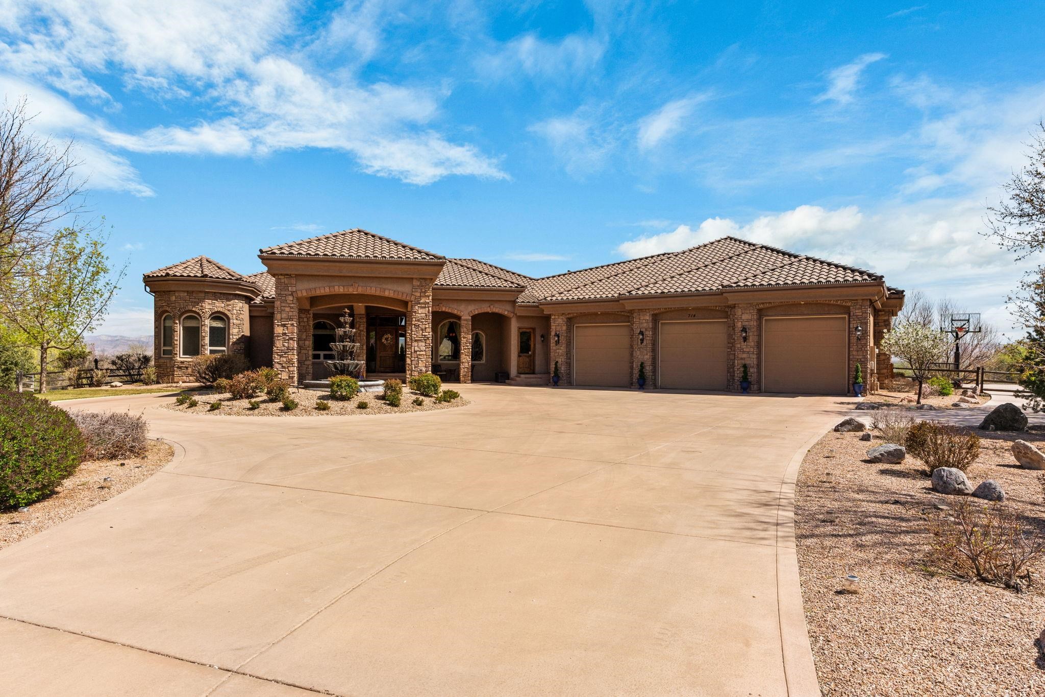 Welcome to 714 Washington Court, a stunning Mediterranean-inspired estate in the prestigious Independence Valley subdivision in Grand Junction’s highly sought-after Redlands area. Situated on a beautifully landscaped one-acre lot, this luxurious home offers breathtaking views of the Colorado National Monument, Bookcliffs, Grand Mesa, and sparkling city lights at night. The exterior impresses with its stone façade, tile roof, arched portico, and circular driveway with a tiered fountain. Inside, the main floor features a spacious living room with soaring ceilings, custom drapery, hardwood floors, and floor-to-ceiling windows that fill the space with natural light. The chef’s kitchen includes Kenmore Elite appliances, a prep sink, wine cooler, walk-in pantry, and a large dining area with mountain views. A formal dining room, office/bedroom, half bath, and luxurious primary suite complete the main level. The primary suite features bay windows, private access to the tiled covered patio, a massive walk-in closet with built-ins, and a spa-like five-piece bath with jetted tub, walk-in shower, and dual vanities. The walk-out basement includes a large family room with a wet bar, theater room with raised seating, three bedrooms, a non-conforming fourth bedroom or gym, and a craft/flex room with a custom craft table. There’s a walk-through full bath between two bedrooms and an additional ¾ bath. Step outside to enjoy a professionally landscaped, terraced yard with multiple staircases, year-round blooms, fruit trees, berry bushes, and a sprinkler/drip system. You can hear a tranquil creek that runs just outside the property line and you’ll frequently spot deer—and even the occasional bald eagle. Enjoy two firepits (one gas, one wood-burning), a trampoline, and outdoor living spaces including a covered patio and upper deck connected by a spiral staircase. The oversized garage offers four bays—three two-car deep—and a dedicated workshop space with sliding automatic doors and built-in cabinetry. Located in one of the area’s most desirable neighborhoods, this property offers a rare combination of luxury, comfort, and natural beauty.