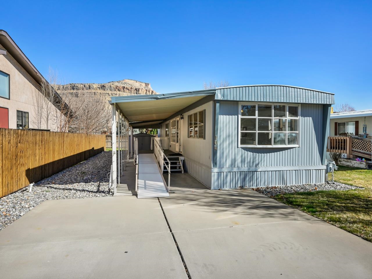 Welcome to this charming retreat in Palisade, Colorado! Nestled in the picturesque Sunset Park community right next to the Colorado River, close to downtown Palisade, and across the main road from Veterans’ Memorial Park, this single wide modular home offers a perfect blend of comfort and convenience. As you step inside, you're greeted by an abundance of natural light that illuminates the entire home, creating a warm and inviting atmosphere. The spacious living room has three large picture windows to enjoy as well as being open to the kitchen and dining room. The flooring features a mix of LVP, carpeting, and durable linoleum in the kitchen. The kitchen has ample built-in cabinetry and counter space, a double wall oven, a pantry, and a gas range, making meal preparation easy. The adjacent dining area has a built-in mirrored sideboard offering an ideal space for enjoying meals. Retreat to the spacious 4-piece full bath, complete with an owned walk-in tub/shower featuring grab bars for added safety and comfort. Both the primary bedroom and the secondary bedroom are bright with large closets. Outside, the landscaped front and backyard welcome you to unwind and soak in the stunning views of The Bookcliffs and Grand Mesa. The outdoor space includes a shed for extra storage and both a covered patio and deck to enjoy. The landscaping is irrigated and cared for through the HOA making this a minimum effort property. With two designated parking spaces, you have easy access to your home. Experience the beauty of Palisade living in this delightful home that combines convenience, comfort, and breathtaking views. Don't miss your chance to make it yours!  There is a $65 fee for the Park application which needs to be completed by the buyer after a signed contract has been received. This is a 55+ community.