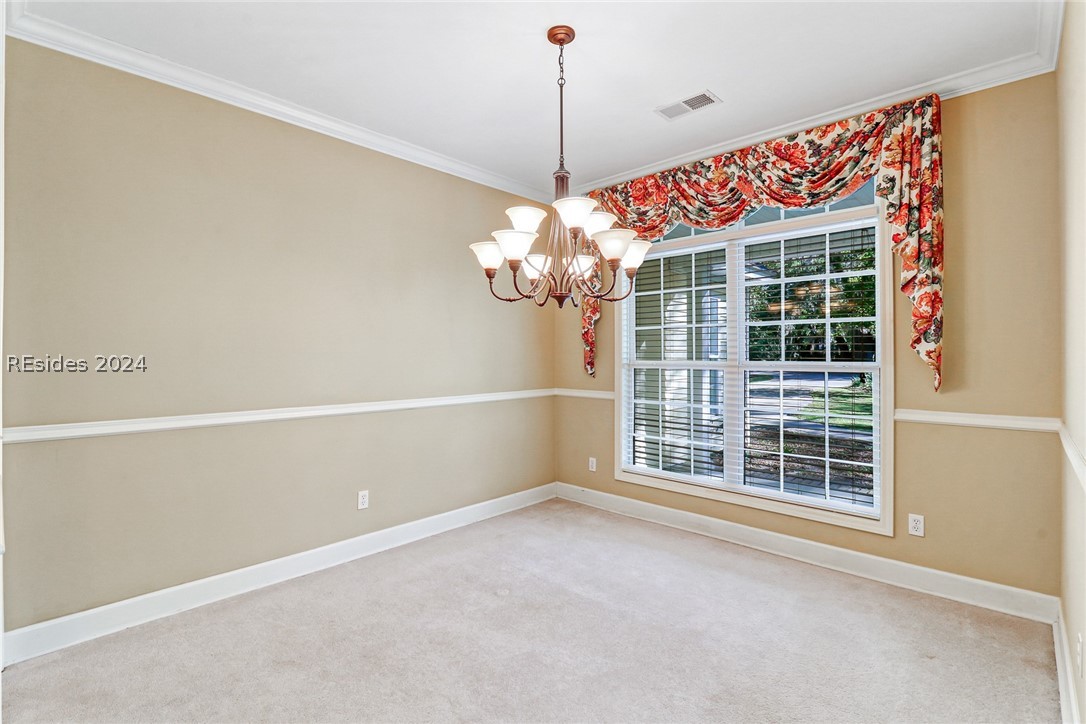 Carpeted spare room featuring crown molding, a notable chandelier, and a wealth of natural​​‌​​​​‌​​‌‌​‌​‌​‌​​​​‌​​​‌‌​‌‌‌ light
