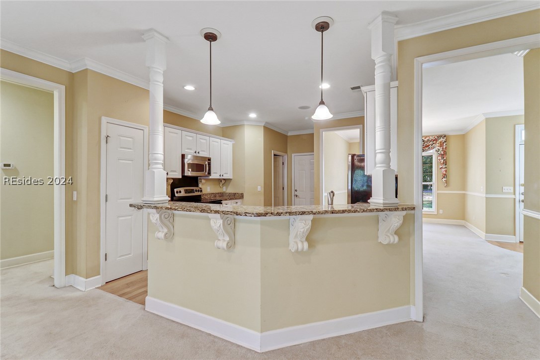 Kitchen featuring decorative light fixtures, light carpet, a kitchen bar, light stone countertops, and white cabinets