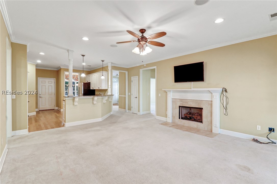 living room with a tiled fireplace, crown molding, and light colored carpet