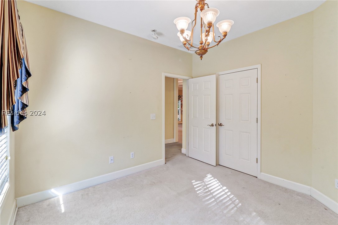 Unfurnished bedroom with light colored carpet and a chandelier