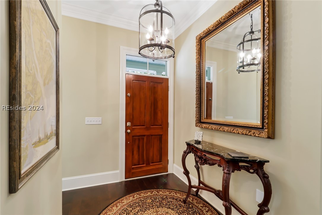 Entryway with dark wood-type flooring, ornamental molding, and a notable chandelier