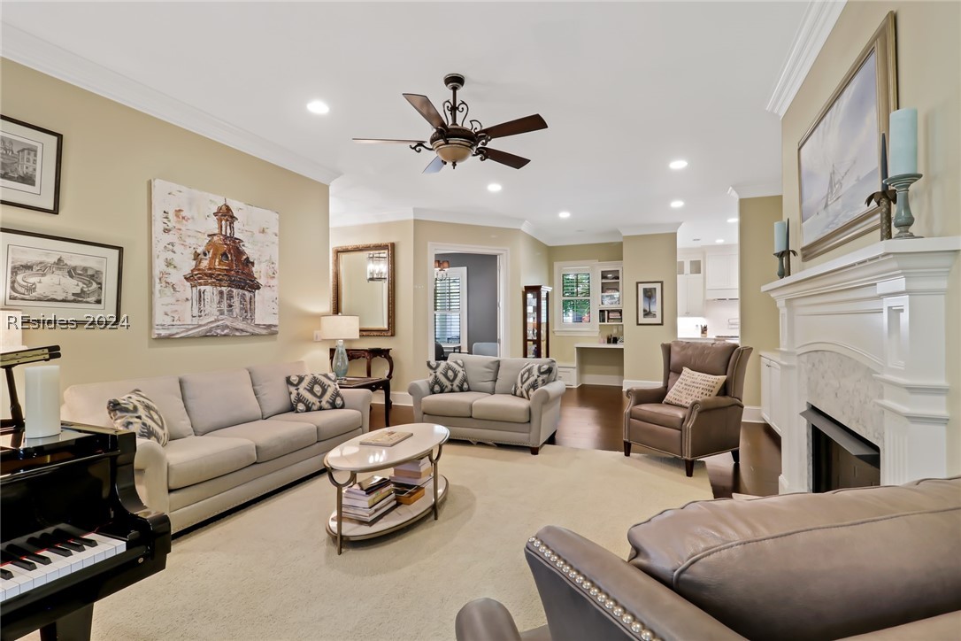 Living room with a premium fireplace, ceiling fan, and ornamental molding