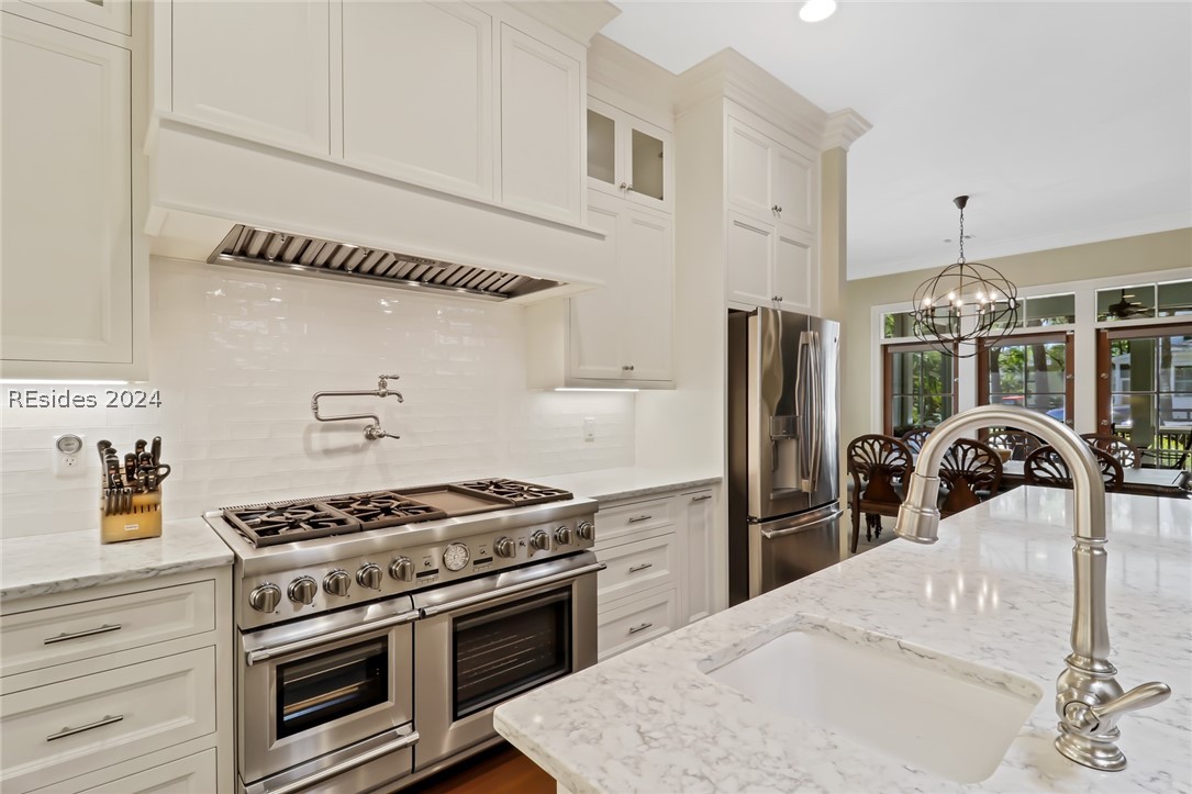 Kitchen featuring appliances with stainless steel finishes, light stone countertops, backsplash, and an inviting chandelier
