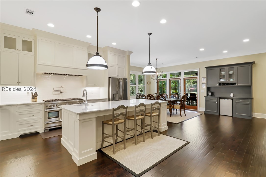 Kitchen featuring hanging light fixtures, gray cabinetry, a kitchen island with sink, a breakfast bar, and stainless steel appliances