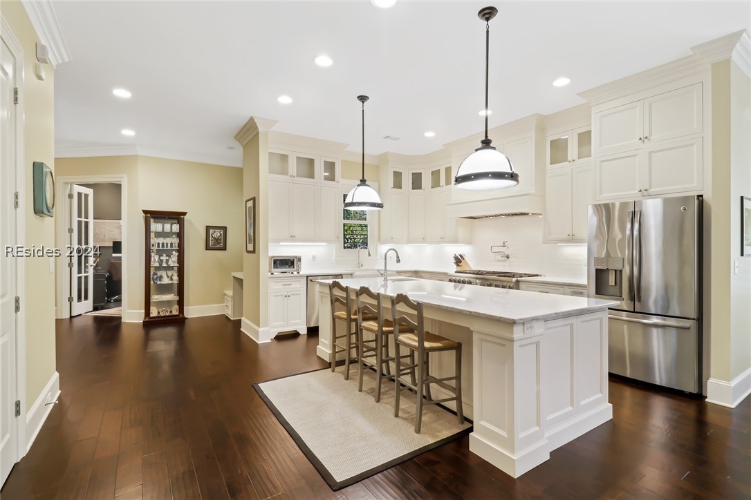 Kitchen with decorative light fixtures, stainless steel appliances, a center island with sink, a breakfast bar area, and ornamental molding