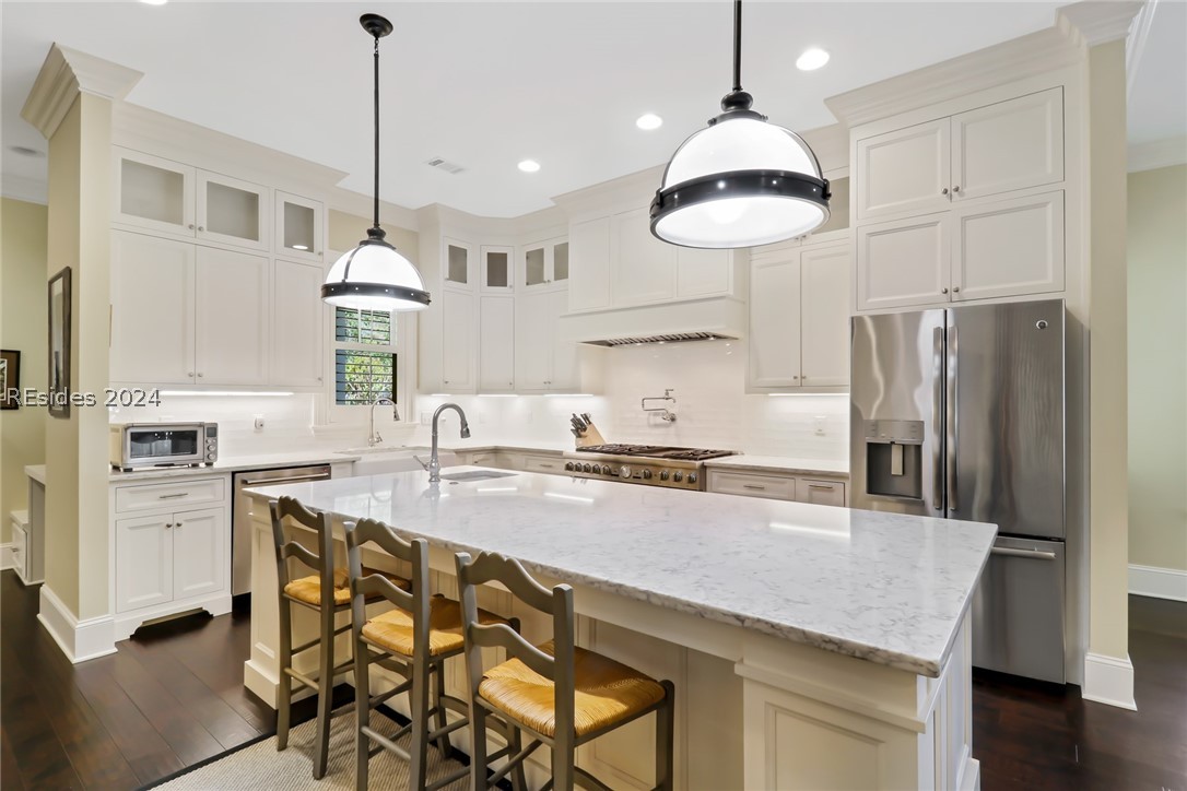 Kitchen with dark wood-type flooring, a center island with sink, a breakfast bar area, stainless steel appliances, and hanging light fixtures