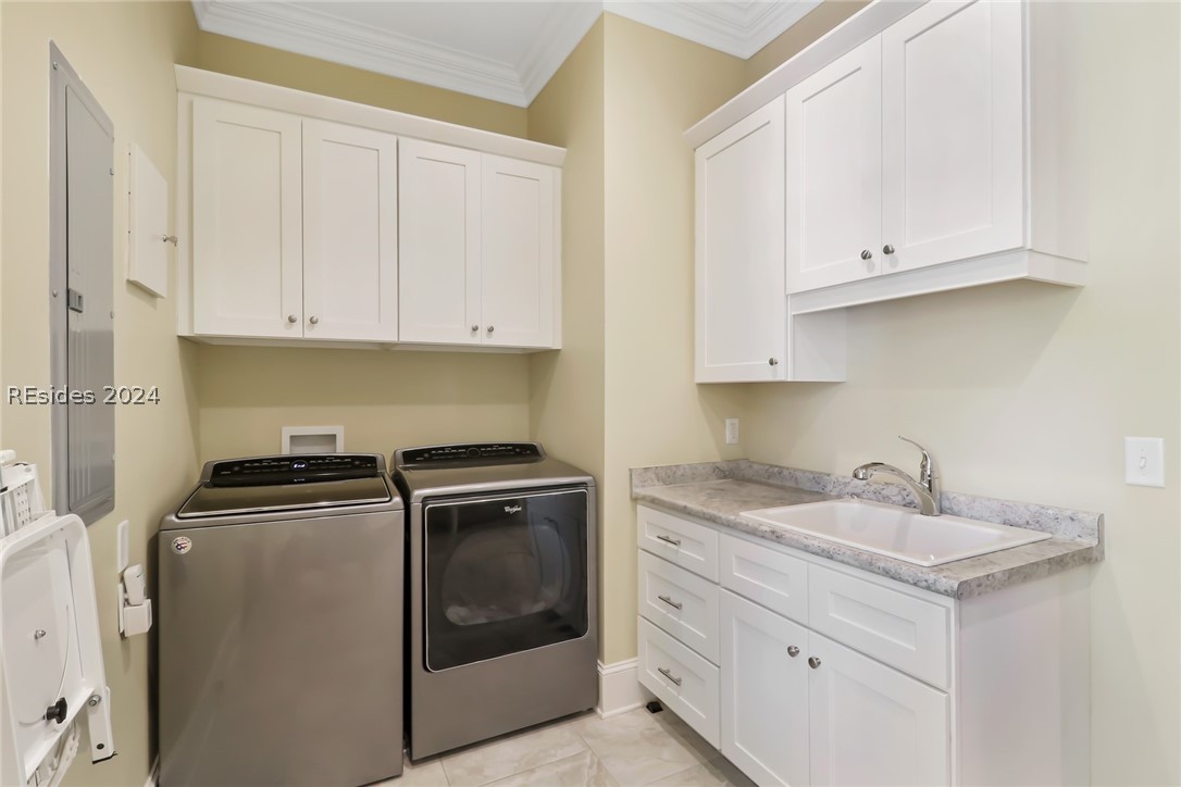 Clothes washing area featuring light tile flooring, cabinets, sink, crown molding, and washing machine and clothes dryer
