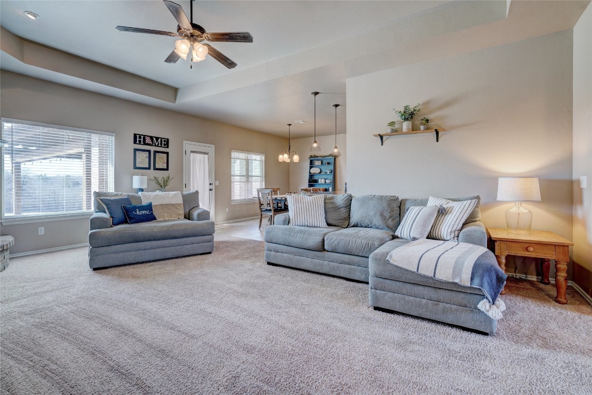 145 Oakridge Drive, Choctaw, OK 73020 carpeted living room featuring a tray ceiling and ceiling fan with notable chandelier