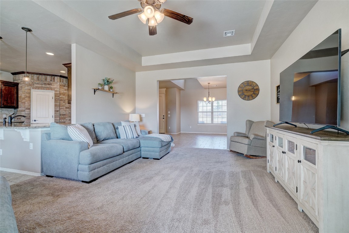 145 Oakridge Drive, Choctaw, OK 73020 living room featuring a tray ceiling, ceiling fan with notable chandelier, light colored carpet, and sink