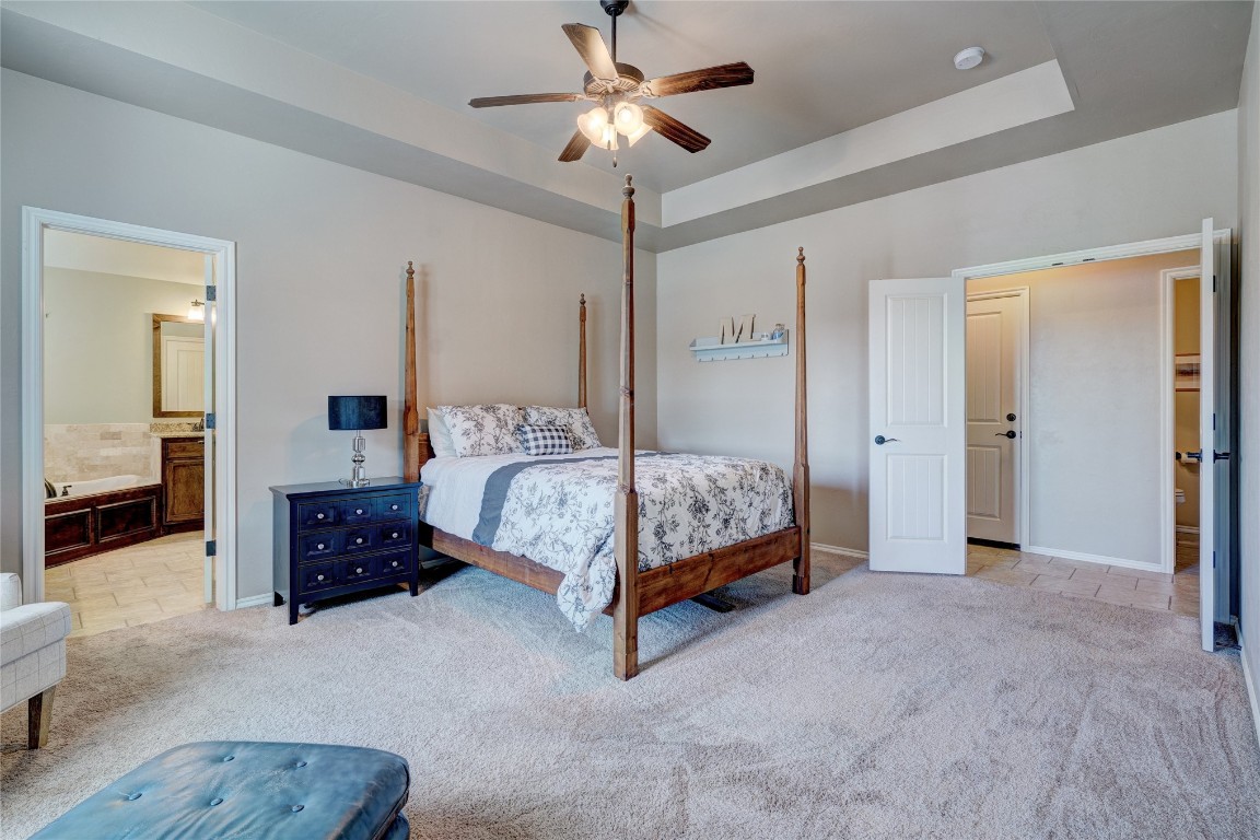145 Oakridge Drive, Choctaw, OK 73020 carpeted bedroom with ensuite bathroom, ceiling fan, and a raised ceiling
