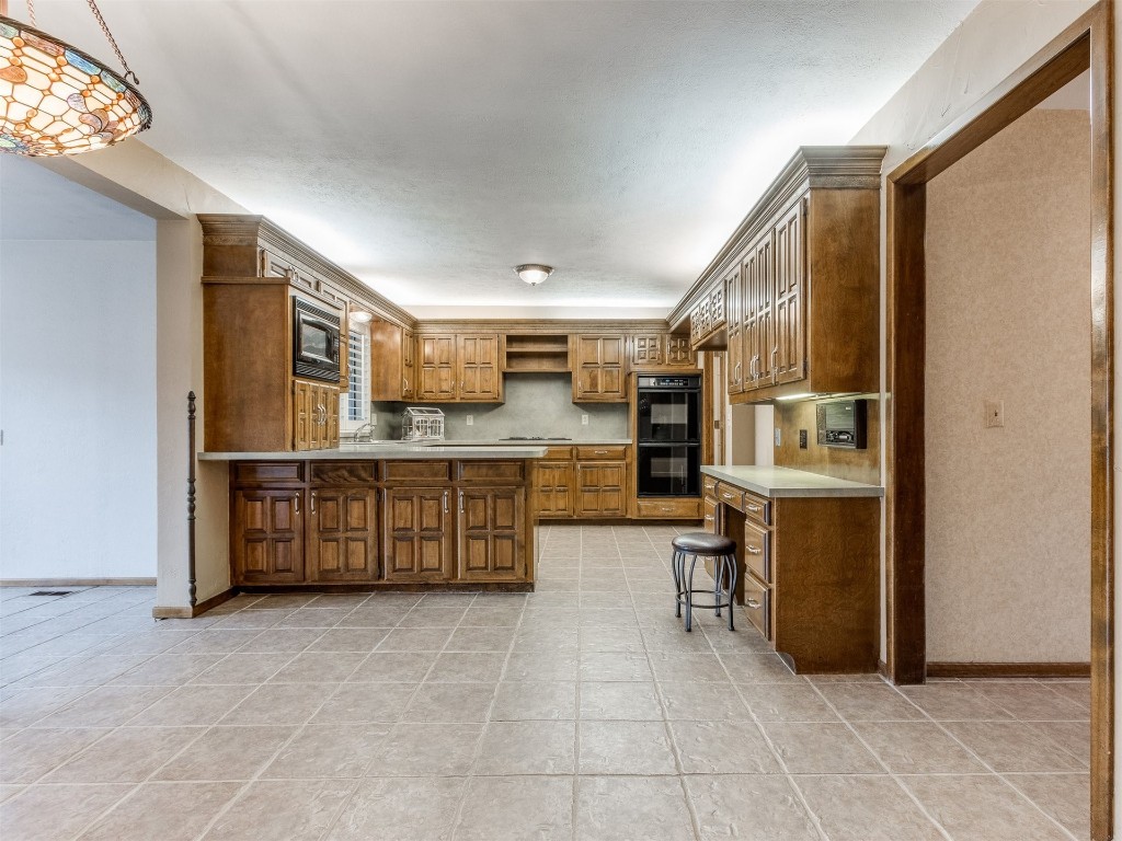 10717 Woodridden, Oklahoma City, OK 73170 kitchen featuring kitchen peninsula, light tile floors, hanging light fixtures, a breakfast bar area, and black appliances