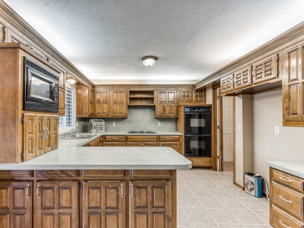10717 Woodridden, Oklahoma City, OK 73170 kitchen with kitchen peninsula, black appliances, light tile flooring, custom exhaust hood, and sink