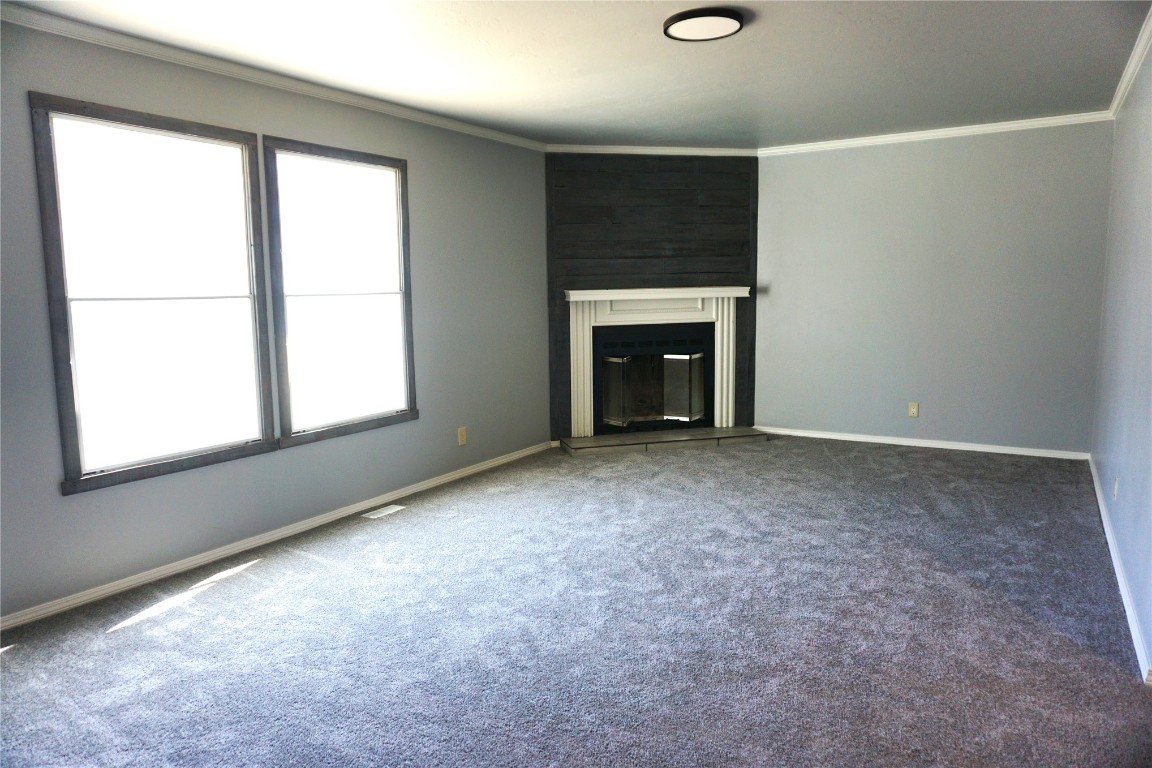 9201 Meadowbrook Lane, Guthrie, OK 73044 unfurnished living room featuring dark carpet, a healthy amount of sunlight, and ornamental molding