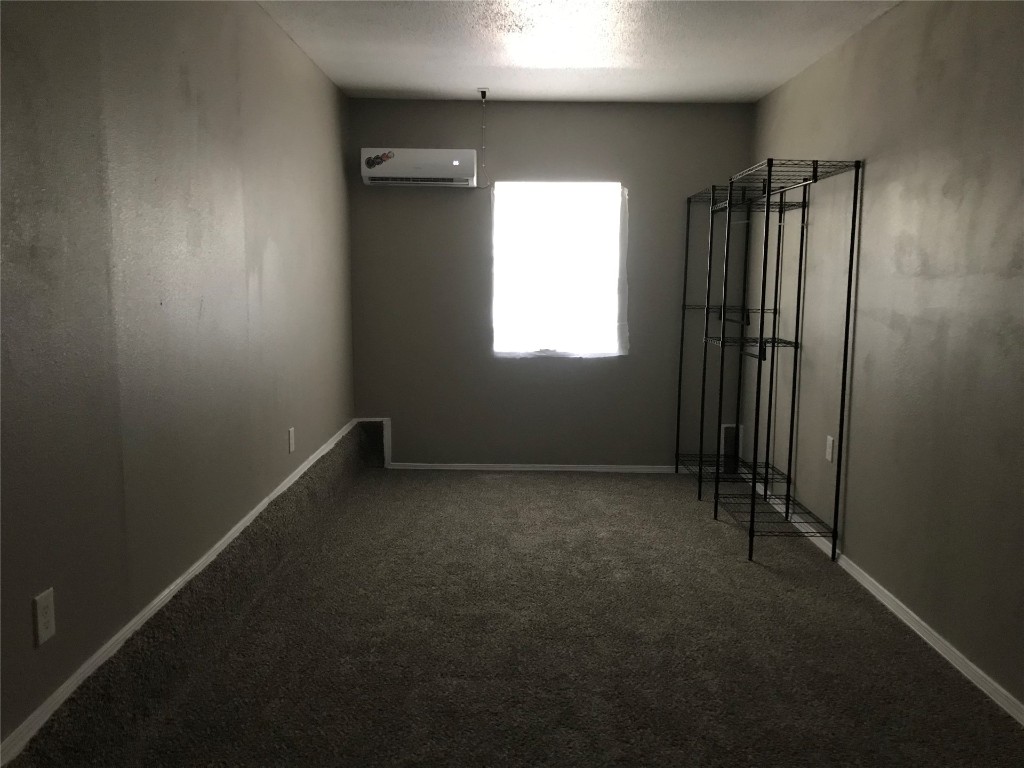 1501 Marydale Avenue, Midwest City, OK 73130 empty room featuring a textured ceiling, dark colored carpet, and an AC wall unit