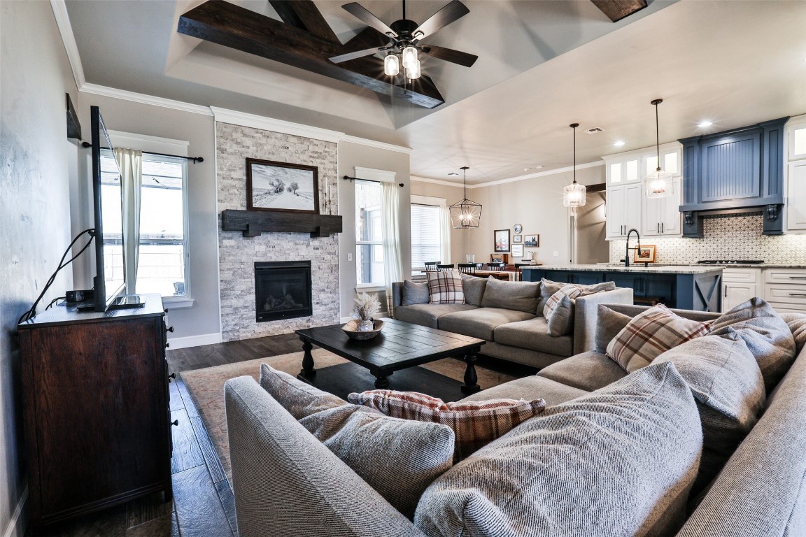 12017 SW 50th Street, Mustang, OK 73064 living room featuring dark hardwood / wood-style flooring, a tray ceiling, ceiling fan with notable chandelier, sink, and a stone fireplace