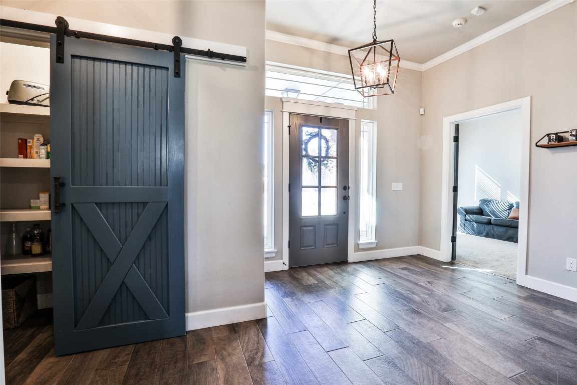 12017 SW 50th Street, Mustang, OK 73064 entryway featuring dark hardwood / wood-style flooring, a barn door, an inviting chandelier, and crown molding