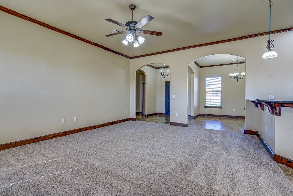 1808 Palomino Drive, Blanchard, OK 73010 unfurnished living room featuring ceiling fan with notable chandelier, crown molding, and dark tile flooring