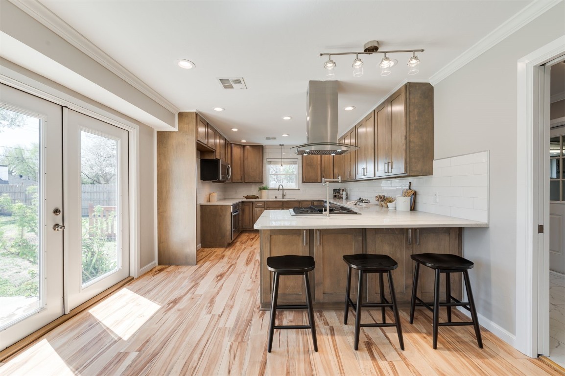 3108 Huntleigh Drive, Oklahoma City, OK 73120 kitchen featuring tasteful backsplash, island range hood, kitchen peninsula, french doors, and light wood-type flooring