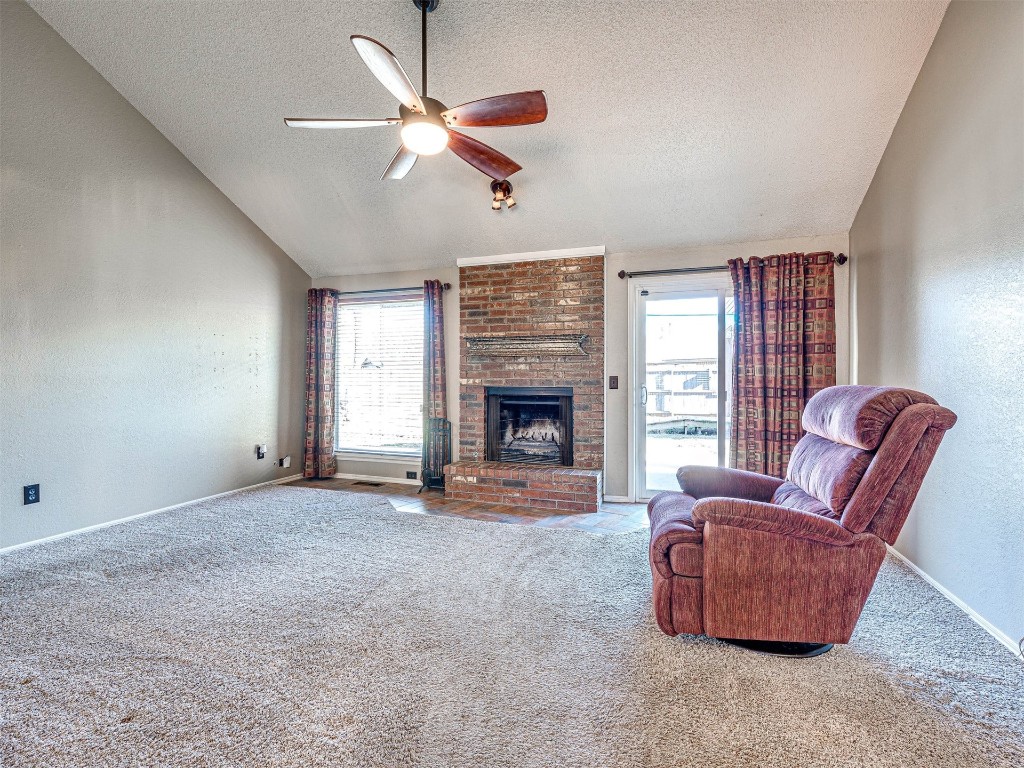 7616 NW 113th Street, Oklahoma City, OK 73162 living room featuring light colored carpet, ceiling fan, a brick fireplace, a textured ceiling, and vaulted ceiling
