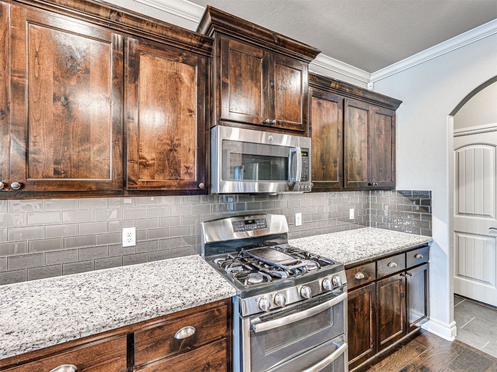 12600 SW 24th Street, Yukon, OK 73099 kitchen featuring appliances with stainless steel finishes, light stone counters, dark hardwood / wood-style flooring, dark brown cabinets, and tasteful backsplash