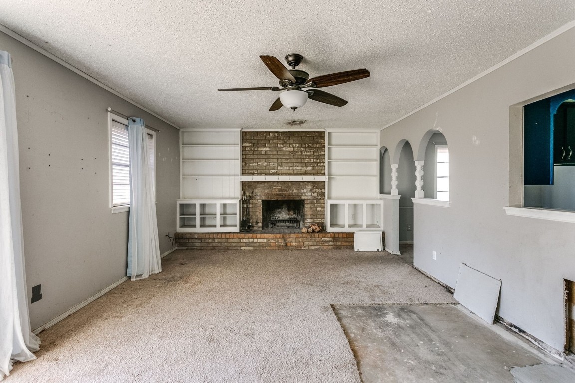 5504 NW 67th Street, Warr Acres, OK 73132 unfurnished living room with a textured ceiling, a fireplace, light colored carpet, built in features, and ceiling fan