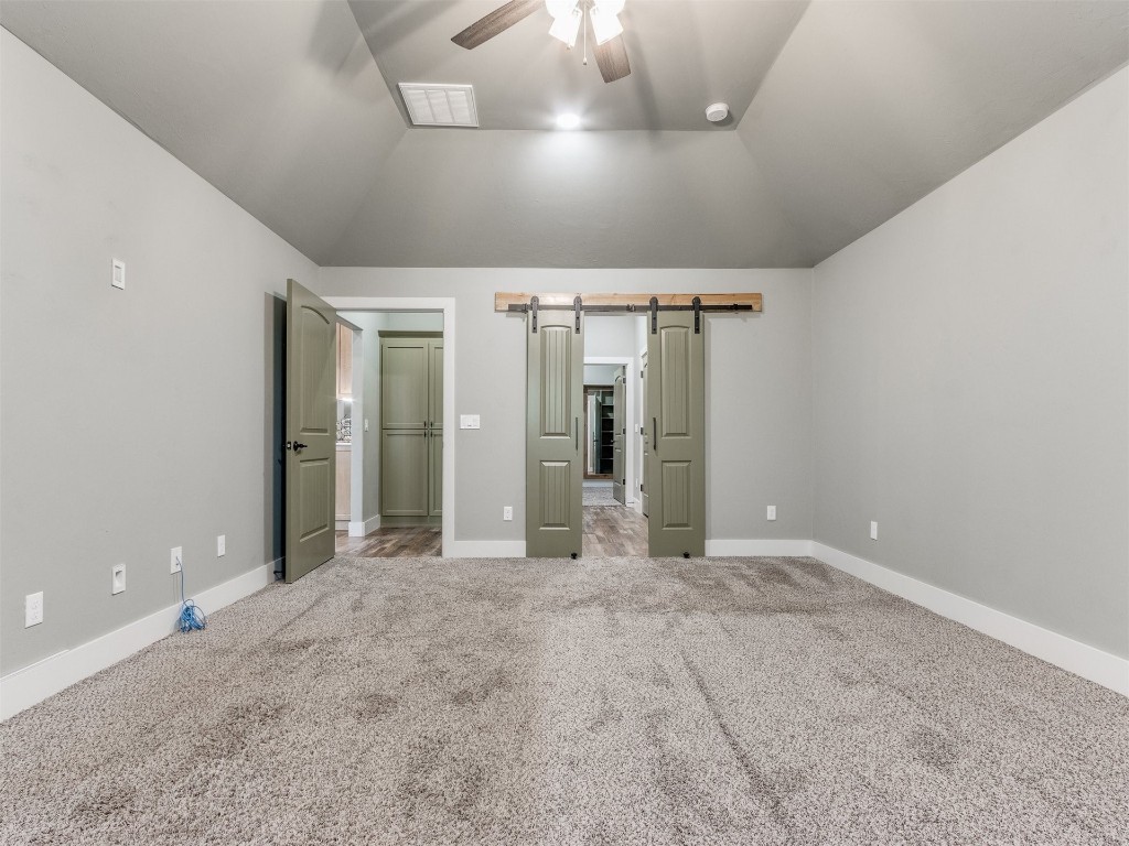 4832 Bermuda Drive, Mustang, OK 73064 unfurnished bedroom with a barn door, ceiling fan, vaulted ceiling, and carpet
