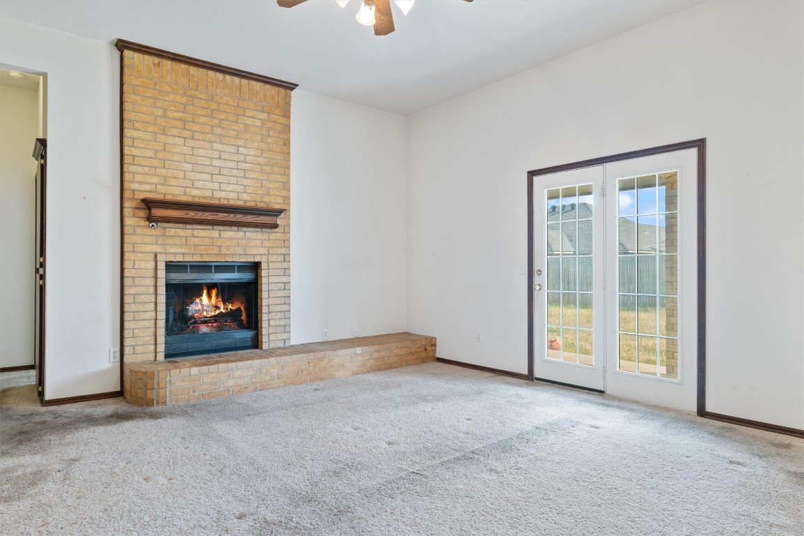12512 SW 13th Street, Yukon, OK 73099 unfurnished living room with a fireplace, brick wall, ceiling fan, and light colored carpet