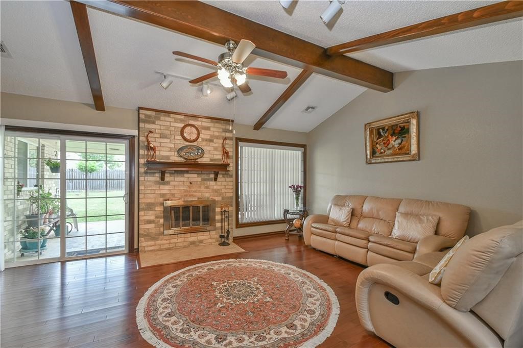 10118 S Kingsgate Drive, Oklahoma City, OK 73159 living room featuring a brick fireplace, ceiling fan, hardwood / wood-style floors, a textured ceiling, and vaulted ceiling with beams