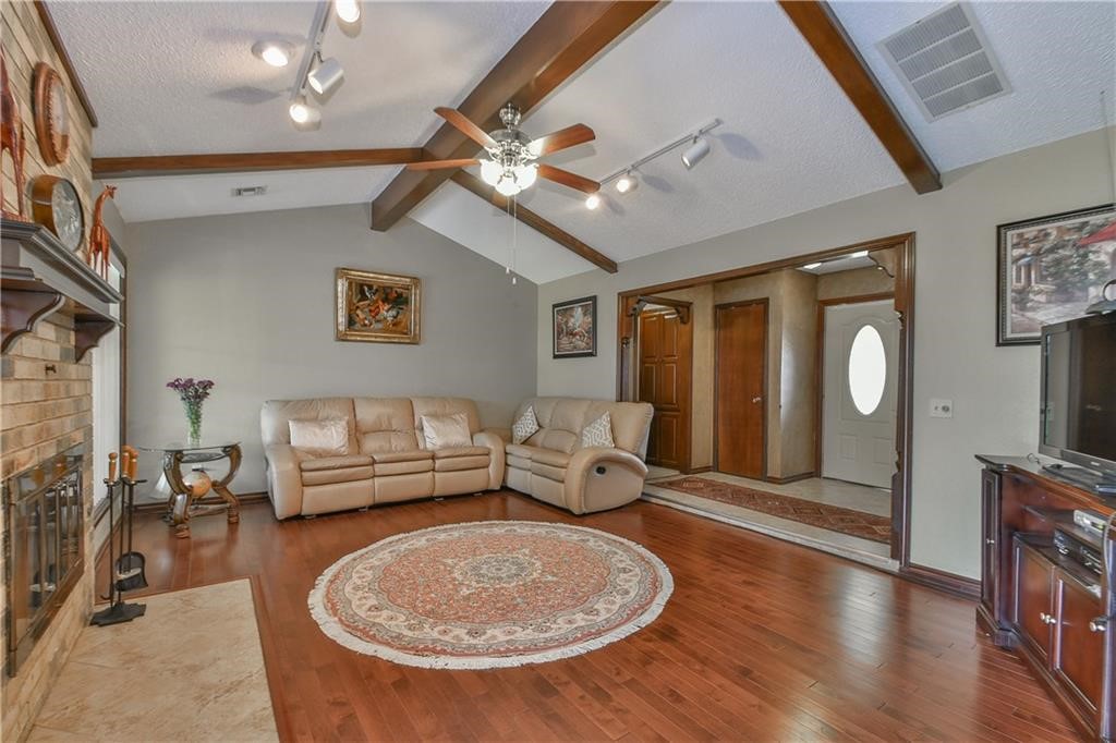 10118 S Kingsgate Drive, Oklahoma City, OK 73159 living room featuring ceiling fan, vaulted ceiling with beams, track lighting, dark hardwood / wood-style flooring, and a textured ceiling