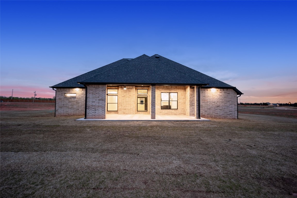 1383 S Gabes Court, Mustang, OK 73064 back house at dusk with a lawn and a patio area