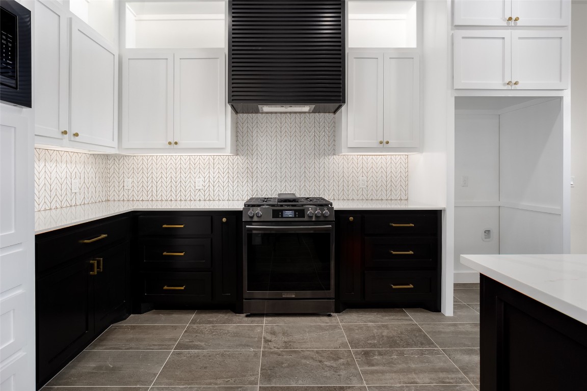 1383 S Gabes Court, Mustang, OK 73064 kitchen featuring dark tile flooring, wall chimney range hood, backsplash, gas range, and white cabinetry