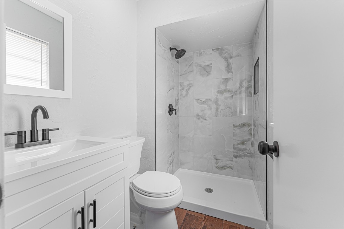 11012 N Mckinley Avenue, Oklahoma City, OK 73114 bathroom with vanity, hardwood / wood-style floors, toilet, and tiled shower