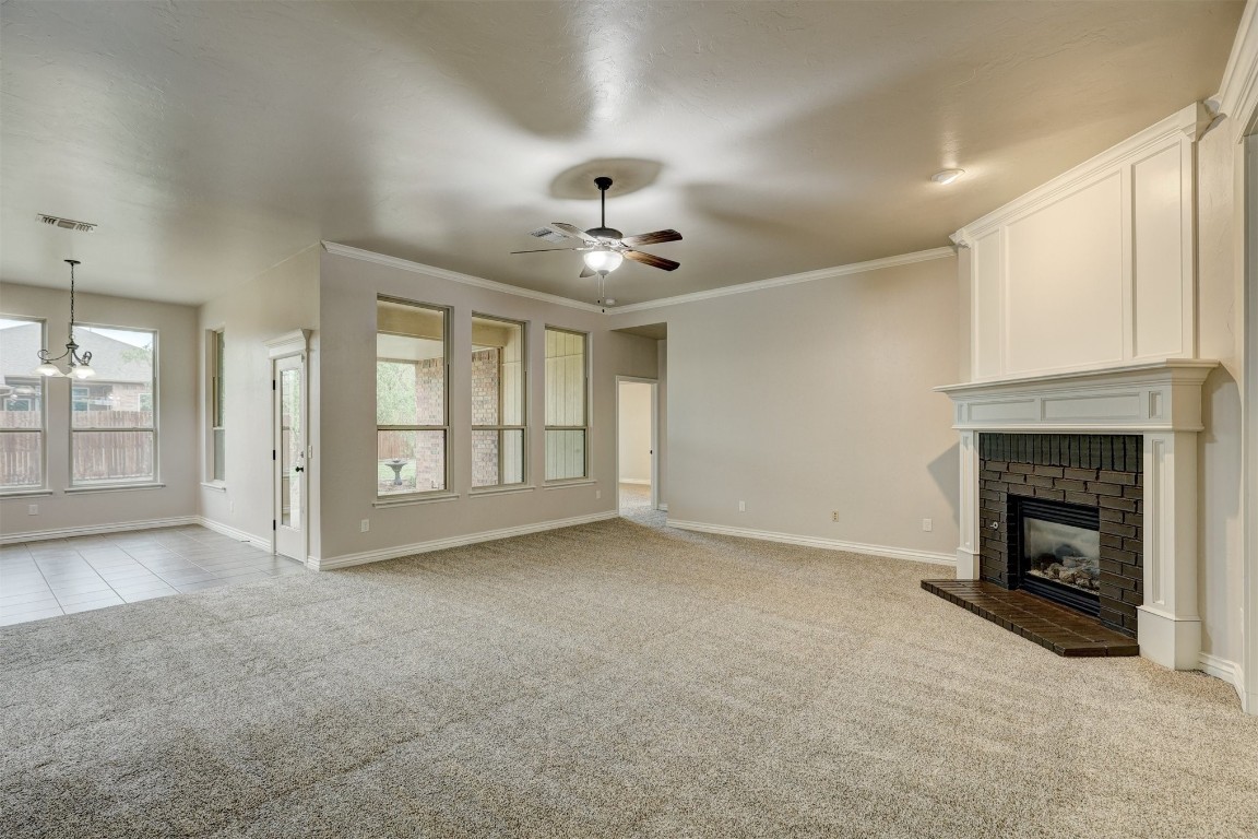 317 Partridge Run Road, Yukon, OK 73099 unfurnished living room with light colored carpet, ceiling fan with notable chandelier, crown molding, and a fireplace