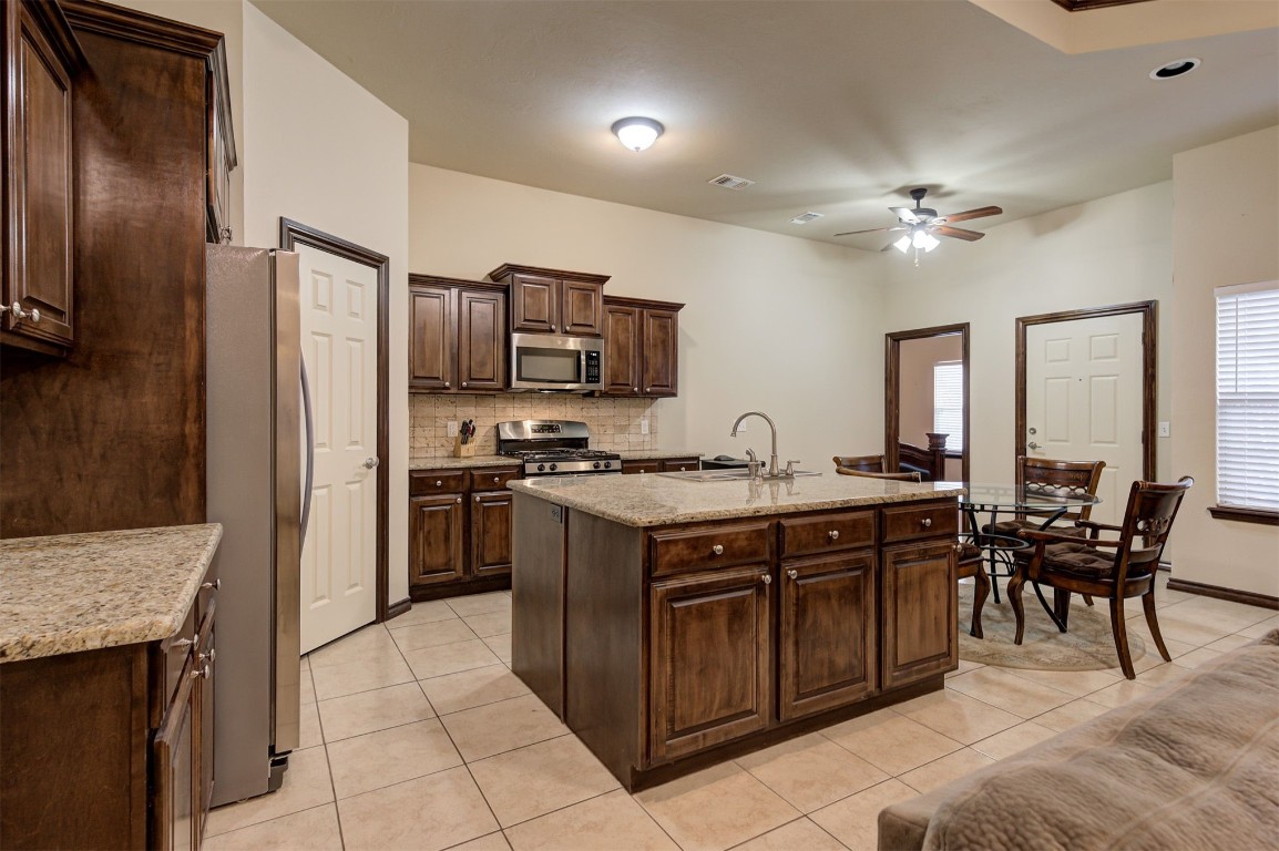 11748 SW 21st Street, Yukon, OK 73099 kitchen featuring appliances with stainless steel finishes, dark brown cabinetry, a center island with sink, light tile floors, and ceiling fan