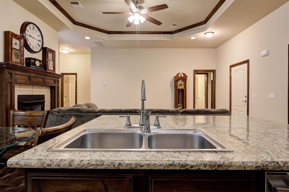11748 SW 21st Street, Yukon, OK 73099 kitchen featuring a tray ceiling, sink, ceiling fan, light stone countertops, and a tiled fireplace
