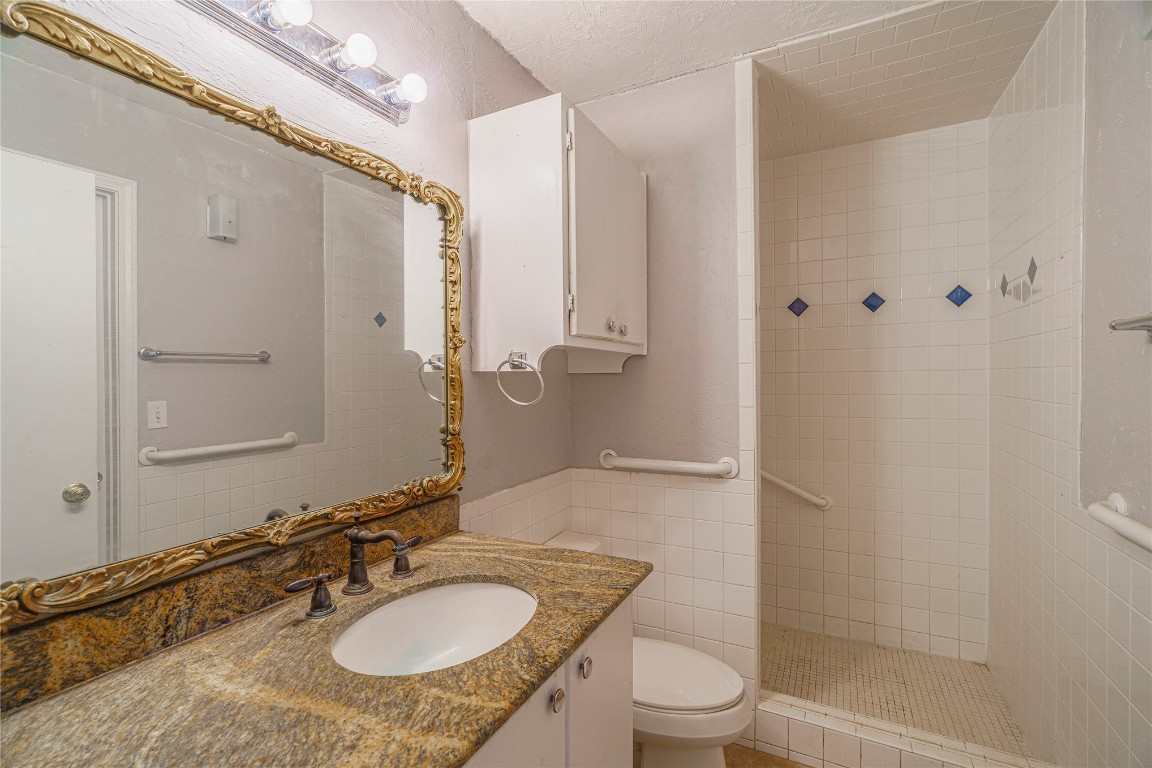 14655 NE 68th Street, Jones, OK 73049 bathroom with a textured ceiling, toilet, tiled shower, and vanity