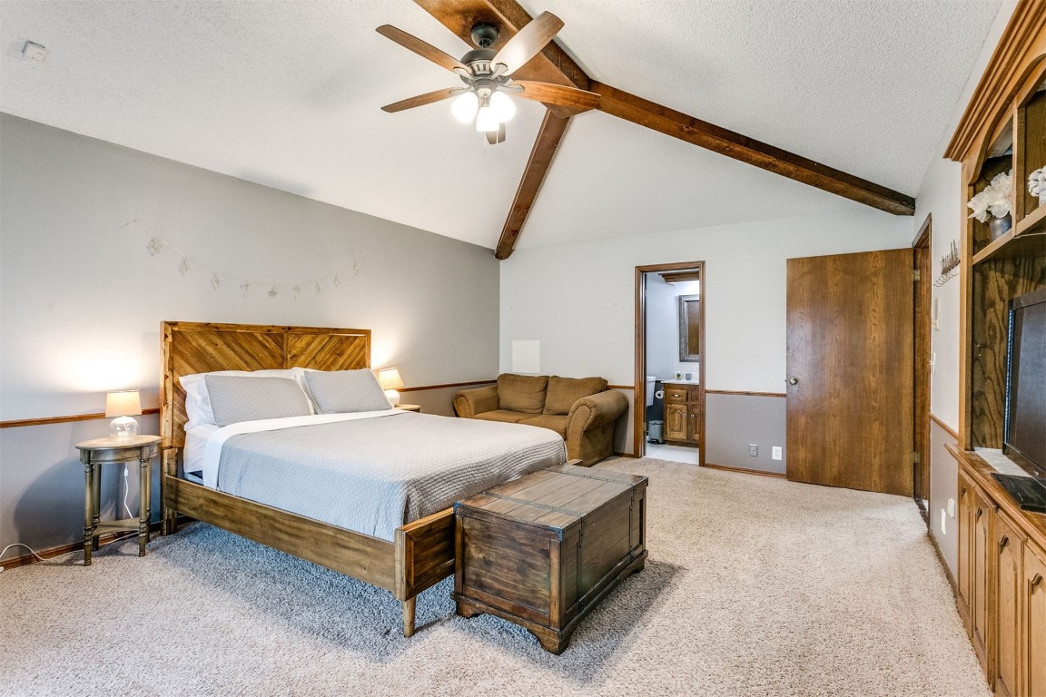 6201 Inland Road, Warr Acres, OK 73132 carpeted bedroom with ceiling fan, vaulted ceiling with beams, connected bathroom, and a textured ceiling