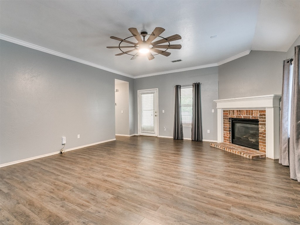 17620 Palladium Lane, Edmond, OK 73012 unfurnished living room featuring ceiling fan, crown molding, light wood-type flooring, and a brick fireplace