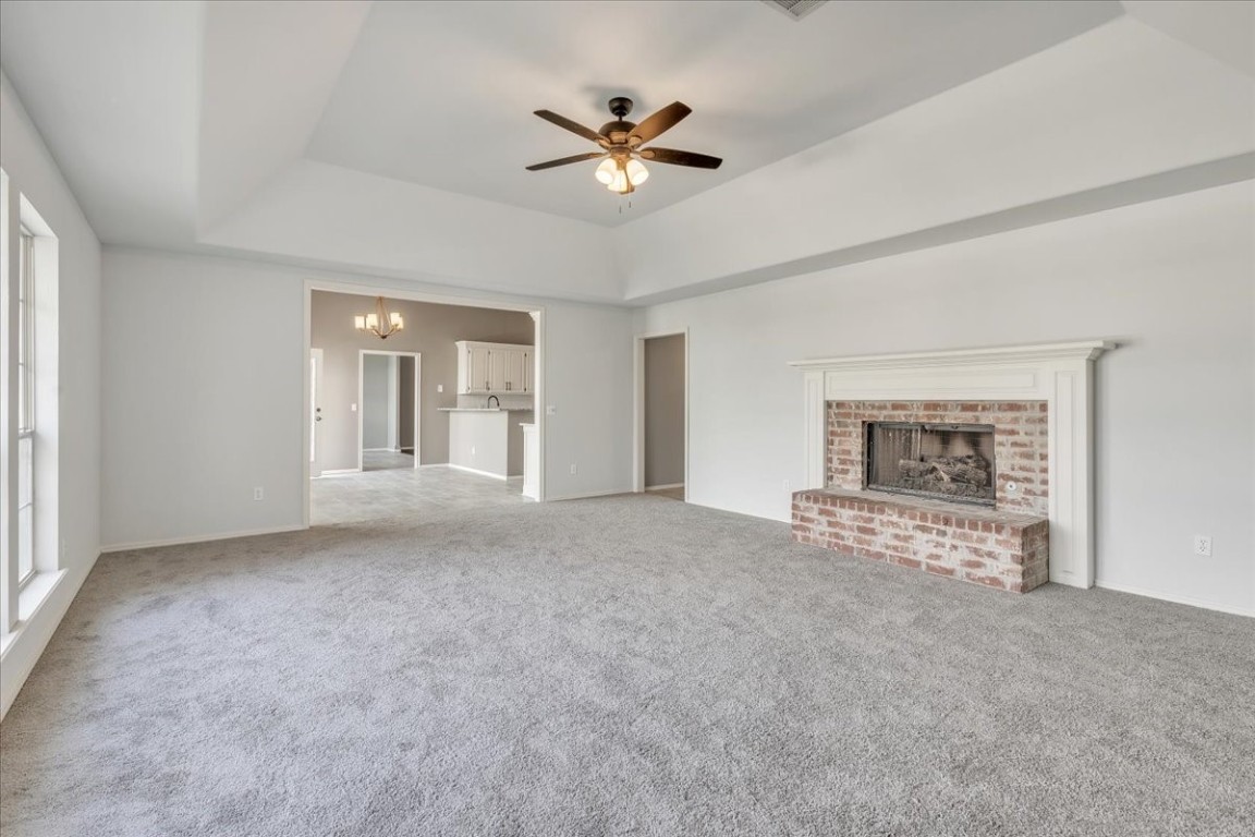12824 Knight Hill Road, Oklahoma City, OK 73142 unfurnished living room with ceiling fan with notable chandelier, light colored carpet, a brick fireplace, and a raised ceiling