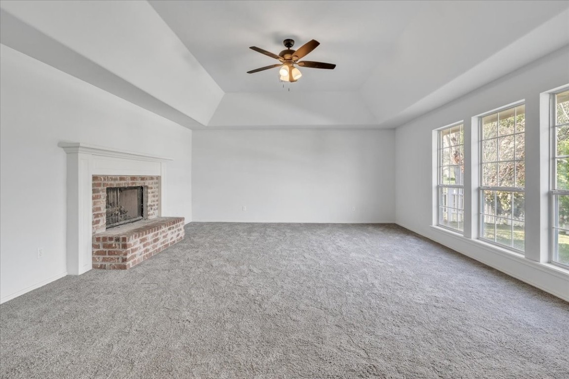 12824 Knight Hill Road, Oklahoma City, OK 73142 unfurnished living room with a healthy amount of sunlight, a brick fireplace, ceiling fan, and carpet floors